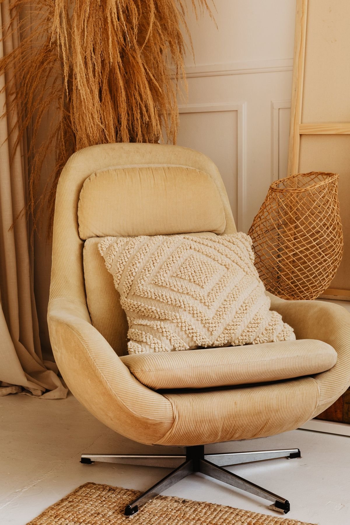 A soft beige armchair with a knitted cushion, a wicker lamp and dried pampas grass