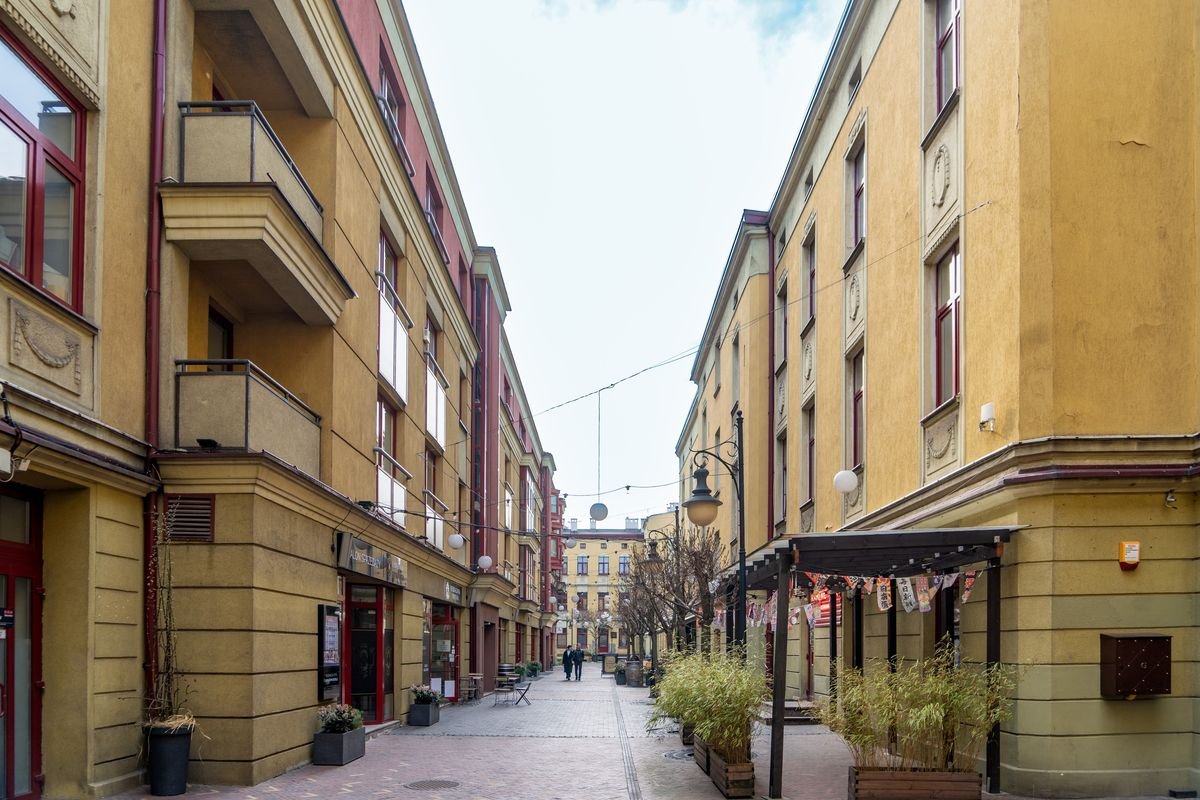 A quiet pedestrian passage off Piotrkowska Street in Łódź with warm yellow façades and plants