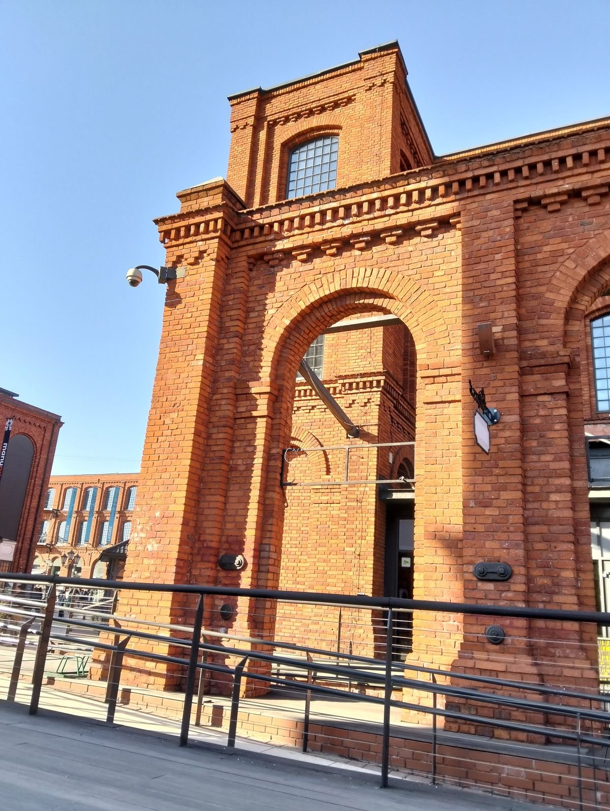 The red-brick entrance gate of Manufaktura in Łódź under a clear blue sky
