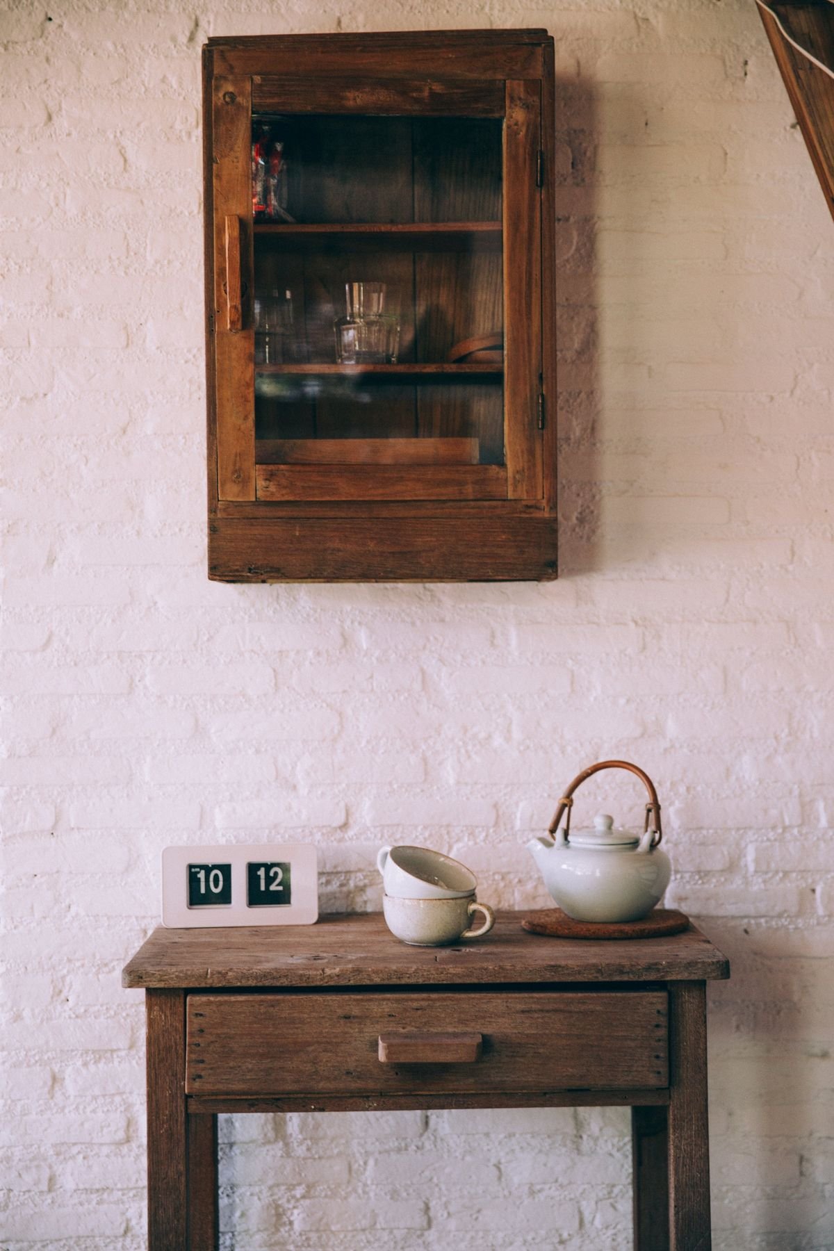 A small wooden side table with a teapot, two cups and a flip clock in a calm, bright room