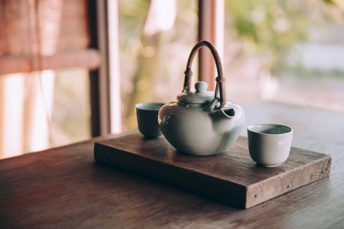 A teapot and two small cups on a wooden board in warm window light