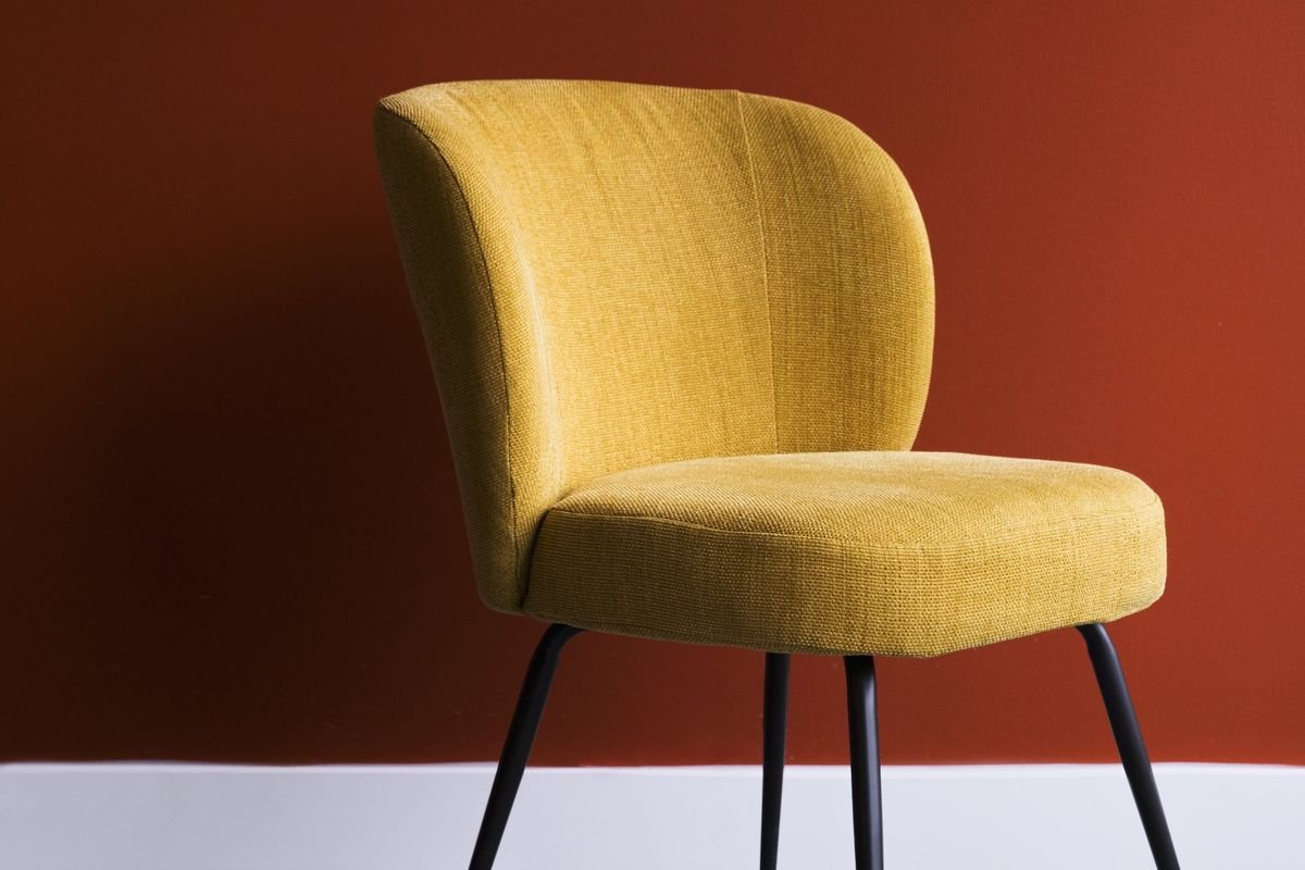 A mustard-yellow upholstered chair against a deep terracotta wall